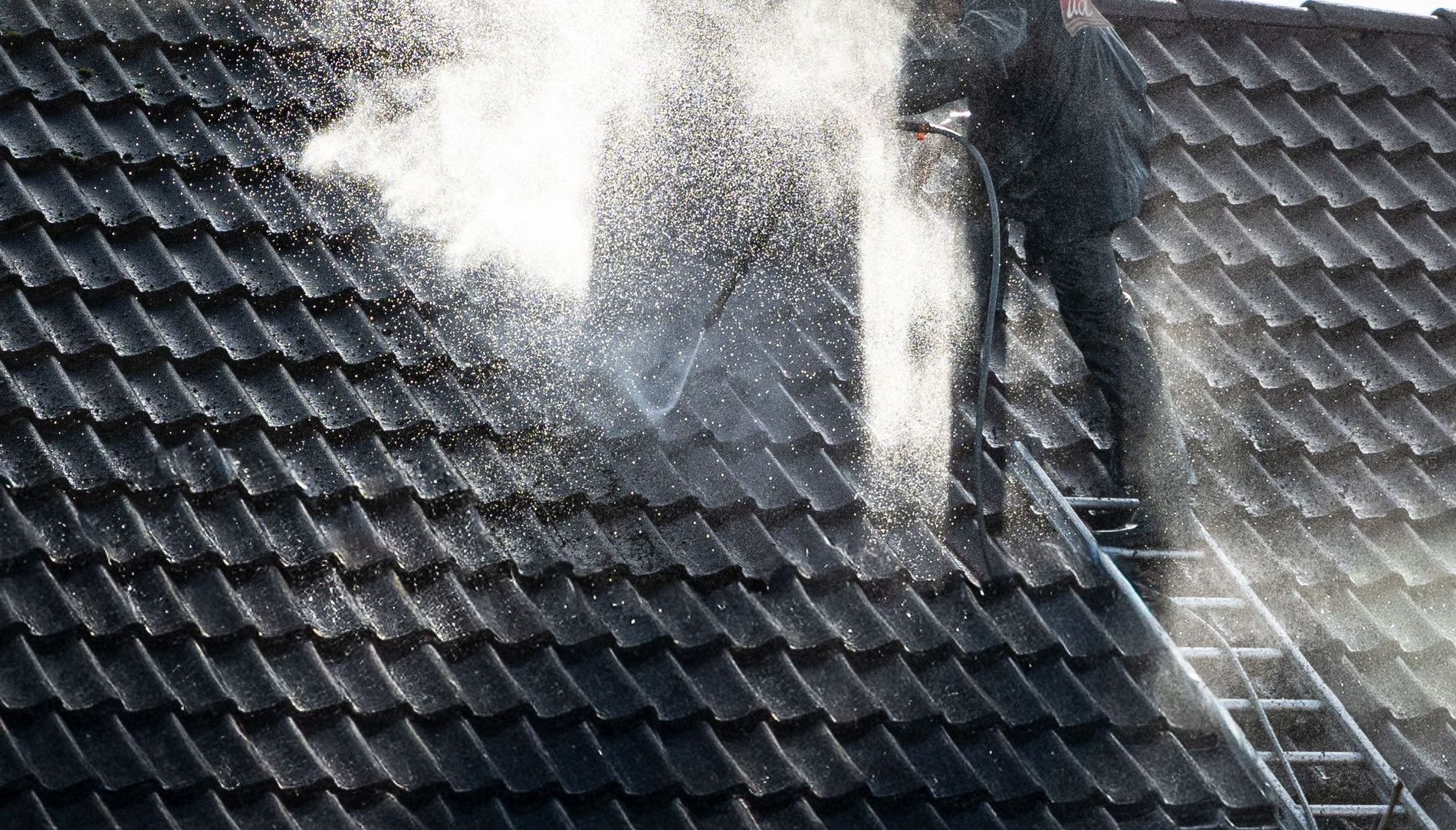 Worker power washing roof tiles, removing grime and buildup.